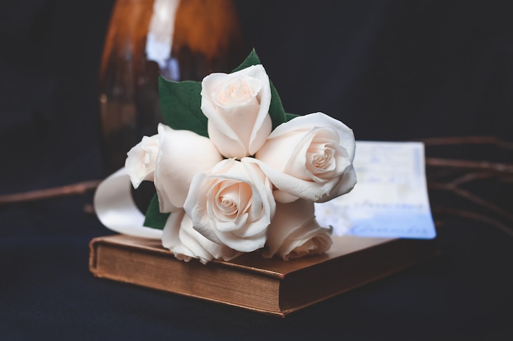 a book resting on a table with a bunch of white roses on it