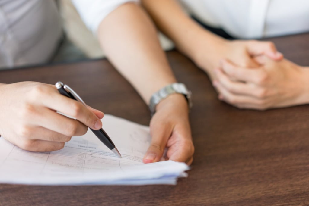 Two individuals are engaged in paperwork, one writing and the other observing